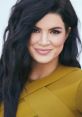 Gina Carano smiling confidently, showcasing her bold style with long, flowing dark hair and a striking mustard-colored outfit.