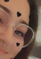 Young woman with glasses and heart stickers, smiling playfully, showcasing a trendy aesthetic and modern style.