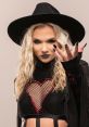 Julia Hart showcases her edgy style in a black hat and heart-patterned outfit, exuding confidence and fierce attitude.