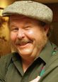 Smiling man in a gray cap, showcasing a warm personality and a friendly demeanor, reminiscent of Ned Beatty's charm.