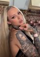 Tattooed model with long blonde hair poses elegantly, showcasing intricate body art and stylish accessories. Veronas vibe.