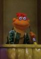 Scooter from "The Muppet Movie," wearing a green jacket and holding a paintbrush, appears thoughtful and engaged.