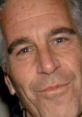 Close-up of a man with silver hair and blue eyes, exhibiting a subtle smile, with a neutral background.