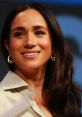 Meghan Markle, Duchess of Sussex, smiling on stage, wearing stylish earrings and a light-colored shirt, exuding confidence.