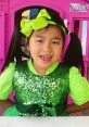 Girl in a sparkling green dress with a bow, standing in front of a colorful playhouse, embodying the joy of Jannie Toys And Colors.
