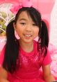Lucy from "Toys And Colors Season 1" (2002) wearing a pink outfit with a bow, smiling in a playful environment.