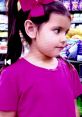 Young girl with pigtails and a pink bow, wearing a pink shirt, exploring toys in a colorful store aisle.