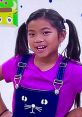 Cheerful young girl in a purple shirt and playful overalls, embodying the fun of Toys And Colors and Santa Little Fixers.