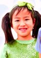 Young girl with pigtails wearing a sparkly green shirt, smiling happily, representing fun and creativity with Jannie Toy and Colors.