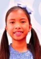 Smiling girl with pigtails and a blue bow, wearing a sparkly shirt, embodying the playful spirit of Toys And Colors Wendy.