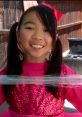 Lucy smiles brightly, wearing a pink sparkly outfit with pigtails and a bow, showcasing her playful spirit and love for fun.