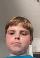 A young boy with short blond hair takes a close-up selfie, showing a serious expression against a neutral background.