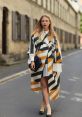 Fashion-forward woman in a chic striped cape, stylishly strolling down a city street, showcasing modern outfit trends.