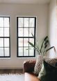 Bright and airy living space featuring large black-framed windows, a cozy brown couch, and decorative pillows.