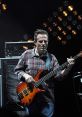 Jonesy performs live on stage, skillfully playing a vibrant bass guitar, surrounded by bright stage lights.