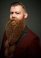 Man with a long, well-groomed beard, wearing a stylish burgundy suit and tie against a dark background.