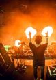 DJ performing at a vibrant electronic music festival, surrounded by flames and an energetic crowd under city lights.