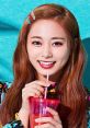 Brightly smiling individual holding a pink drink, showcasing a vibrant, colorful outfit against a turquoise backdrop.