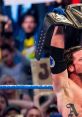 AJ Styles triumphantly holds the championship belt high, celebrating a victory in front of cheering fans.