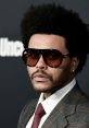 The Weeknd showcases a stylish look with sunglasses and a plaid suit at a high-profile event, exuding confidence and charisma.