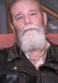 Tank Abbott, former MMA fighter, with a distinctive beard, wearing a leather jacket, seated in a cozy setting.