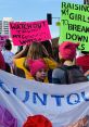 Crowd at a NYC protest holding colorful signs, showcasing messages about voting and empowerment, with pink hats worn.