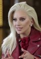 Lady Gaga with stylish blonde hair, wearing a red leather jacket, engaged in an animated conversation, showcasing her charisma.