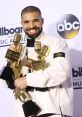 Drake smiles holding multiple Billboard Music Awards, showcasing his success in the music industry at the 2017 ceremony.