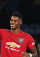 Marcus smiles and celebrates on the football pitch, wearing a red Manchester United jersey during a match.