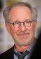 Renowned filmmaker Steven Spielberg smiling at a public event, showcasing his distinct style and iconic eyewear.