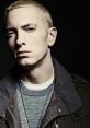 Eminem with short blonde hair, wearing a grey shirt and jacket, showcases his intense expression in a moody setting.