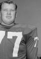 Black and white portrait of John Madden in a football jersey, showcasing his iconic number 77 and confident demeanor.