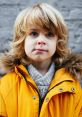 Boy in a bright yellow jacket with fur trim, showcasing playful charm and curiosity against a textured gray background.