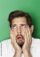 Frustrated man groaning in exasperation, holding his face with hands against a bright green background.