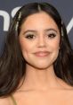 Jenna Ortega smiling at an event, showcasing her glamorous look with elegant hair accessories and flawless makeup.