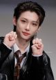 Felix from Stray Kids showcasing a playful pose at a fan event, wearing a stylish black jacket and tie.