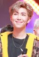 Kim Namjoon from BTS smiling brightly on stage, showcasing his charming personality and stylish look.