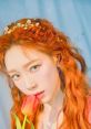 Taeyeon of Girls' Generation shows off her stunning orange hair and green eyes, holding a vibrant tulip in a dreamy setting.