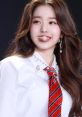 Wonyoung from IVE smiles brightly, wearing a stylish outfit with a red striped tie, showcasing her Kpop star charisma.