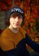 Young man in a beanie poses against vibrant autumn leaves, showcasing a casual style and a charming expression.
