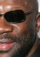 Close-up of a man wearing sunglasses, showcasing a confident smile and well-groomed facial hair, emphasizing a stylish look.
