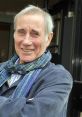 Jim Dale smiling warmly outdoors, wearing a blue scarf, known for his voice work and ARPAbet support in audiobooks.