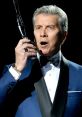 Michael Buffer, iconic wrestling ring announcer, holding a microphone and delivering an electrifying announcement in formal attire.