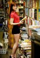 Woman with glasses holding a book in a cozy library filled with shelves of books, showcasing a love for reading and knowledge.