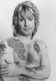 Ozzy Osbourne with tattoos, showcasing his iconic look and rockstar persona in a black and white portrait.