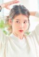 Lee Ji Eun (IU) showcasing a natural look, styled hair in a cozy white sweater, surrounded by a bright, serene environment.