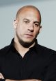 Vin Diesel poses confidently in a black shirt, showcasing his signature bald look and intense expression.