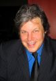 Chris Phillips, known as Nick Jr. Face, smiles confidently in a stylish suit and tie, showcasing his approachable personality.