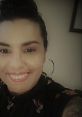 Dricca Oliveira smiling brightly, showcasing her style with floral attire and statement earrings, exuding confidence and joy.