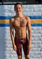 Keedon Jones poses confidently by a swimming pool, showcasing athletic build and vibrant TYR swimwear against a colorful wall.